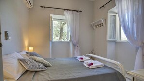 Un dormitorio con una cama, dos ventanas con cortinas, una mesita de noche y una estantería en la pared.
