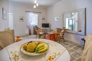 A room with a dining table set with fruit, wicker chairs, a television, and a large mirror.