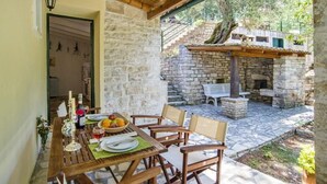 Un área de comedor al aire libre con paredes de piedra, mobiliario de madera y chimenea de piedra.