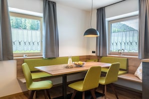 A dining area with a wooden table, green upholstered chairs, and a pendant light.