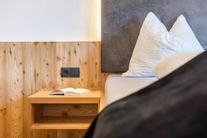 A wooden bedside table with a book, a power outlet, and a bed with pillows.