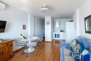 Un salon moderne comprenant un canapé, une table à manger avec des chaises, un coin cuisine et un téléviseur fixé au mur.