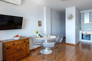 Une cuisine moderne dotée d’un four encastré, un coin repas avec une table ronde et des chaises, et un téléviseur fixé au mur.