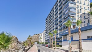 A coastal road with a multi-story building, palm trees, and a pedestrian crossing sign. - Vacation Apartment 'Epsilon 2 4f Primera Línea De Playa' with Sea View & Shared Pool (Almuñecar)