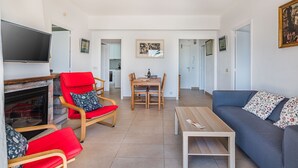 A living room with a fireplace, red and blue furniture, a TV, and a dining area. - 'Pine Walk' Apartment with Sea Views, Wi-Fi and Air Conditioning (Pollensa)