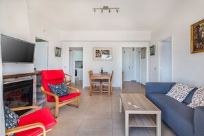 Un salon avec une cheminée, des meubles rouges et bleus, un téléviseur et un coin repas.