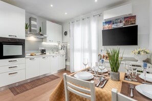 Uma cozinha moderna com armários brancos, forno embutido e sala de jantar preparada para seis pessoas, com mesa, cadeiras e um vaso de flores.