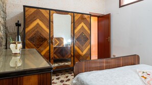 Un dormitorio con una cama, un armario de madera con espejo y una mesita con un florero.