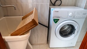 Un baño con un inodoro blanco, un portaescobillas de madera y una lavadora blanca.