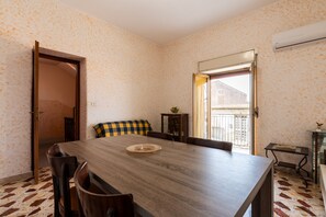 A dining area with a wooden table, chairs, a checkered cushion, and a view through an open door.