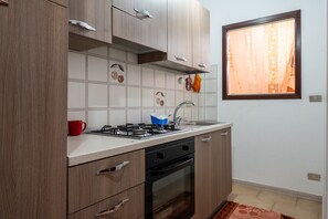 A kitchen with wooden cabinets, a gas stove, a sink, and a window with curtains.