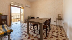 Un comedor con mesa y sillas, un banco, una mesita auxiliar y vistas a través de una puerta abierta.