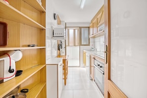 A narrow kitchen with wooden cabinets, a built-in oven, and a microwave.
