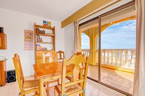 A dining area with a wooden table and chairs, a bookshelf, and a large window with a view of the sea. - Holiday Apartment 'Barlovento I' with Sea View, Terrace, Shared Pool & Wi-Fi (Xeraco)