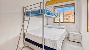A bunk bed room with a ladder, a bedside table with a lamp, and a window with a view of buildings. - Holiday Apartment 'Barlovento I' with Sea View, Terrace, Shared Pool & Wi-Fi (Xeraco)