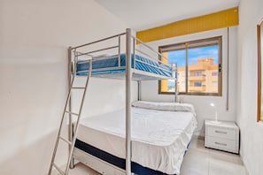 A bunk bed room with a ladder, a bedside table with a lamp, and a window with a view of buildings.