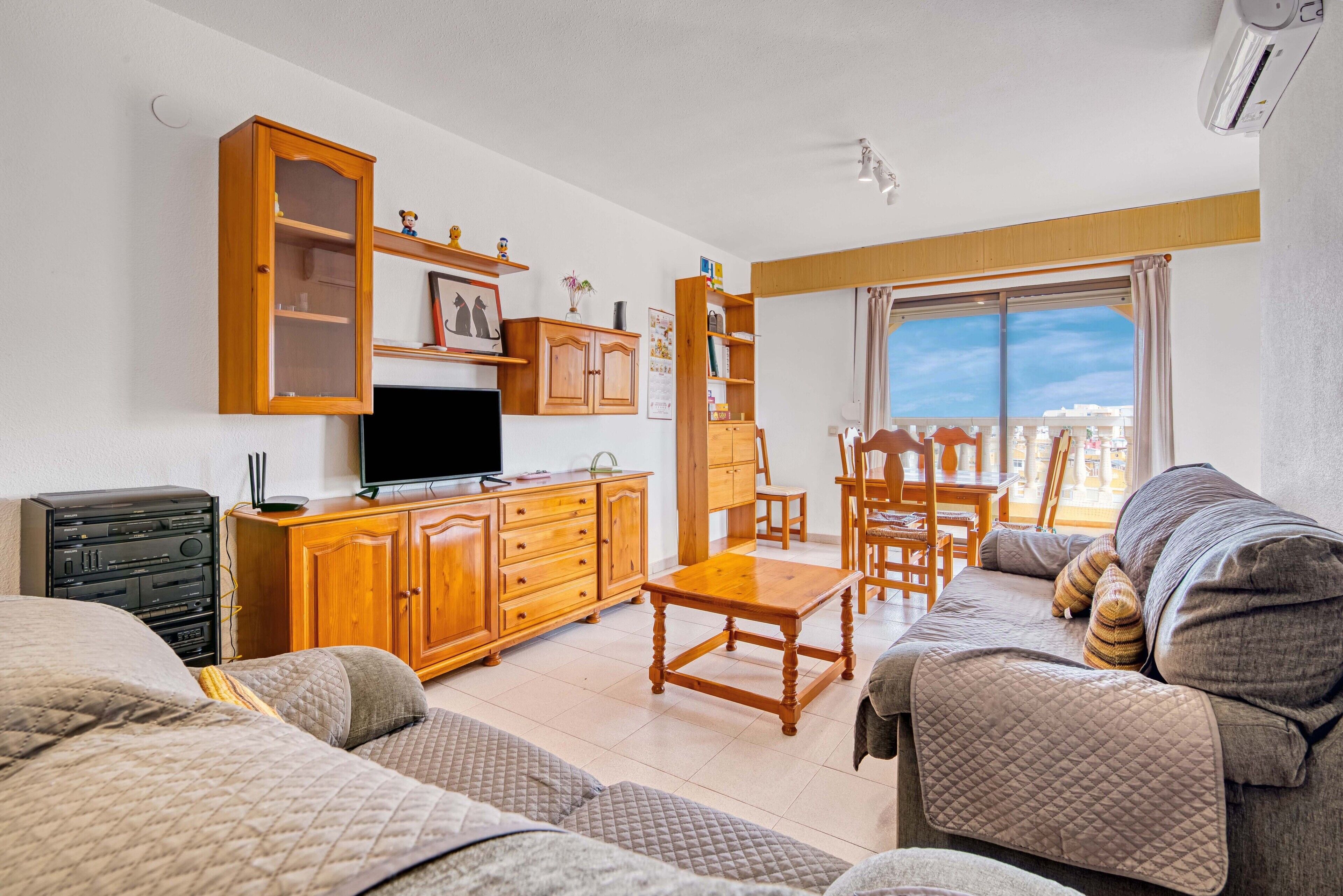 Una sala de estar con sofá, televisión, mueble de madera y un comedor con sillas.