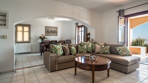 A living room with a sofa, coffee table, and a dining area with chairs and a table. - Villa 'Kumusha' with Sea View, Pool, Garden & Wi-Fi (Kefalonia)
