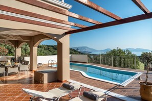 Un espace piscine sur le toit avec vue sur les montagnes, un coin salon couvert et un bar au bord de la piscine.
