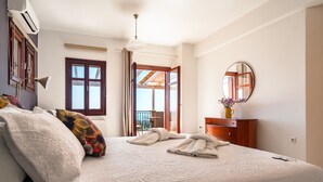 A hotel room with a large bed, a wooden dresser, a round mirror, and a view through an open door. - Villa 'Kumusha' with Sea View, Pool, Garden & Wi-Fi (Kefalonia)
