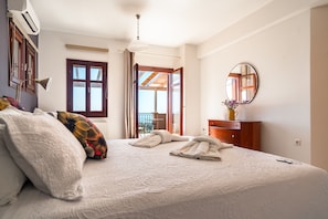 Une chambre d’hôtel avec un grand lit, une commode en bois, un miroir rond et une vue sur l’extérieur, visible à travers une porte ouverte.