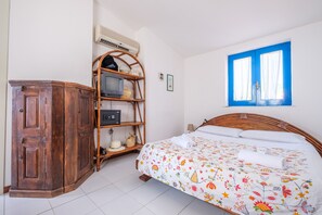 A bedroom with a bed, a wardrobe, a shelf unit, a window, and an air conditioning unit.
