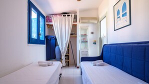 A bedroom with two beds, a wardrobe, a window with blue shutters, and a picture on the wall.