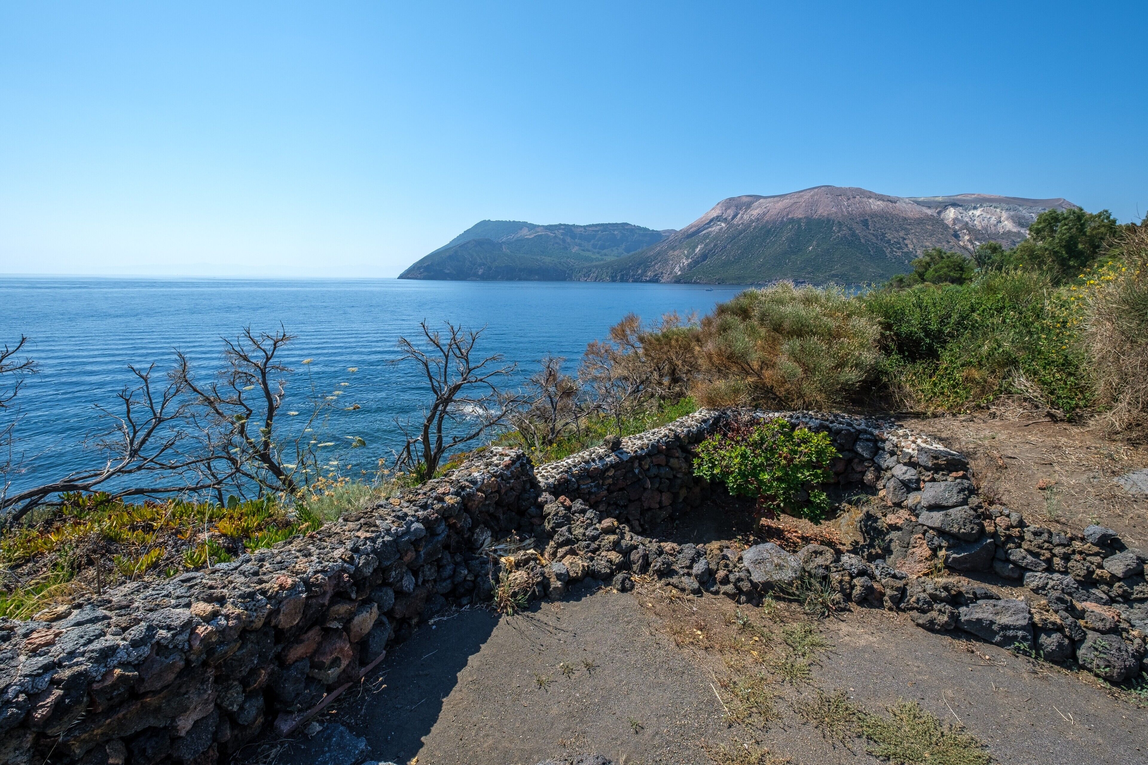 A coastal landscape with a stone wall and vegetation.