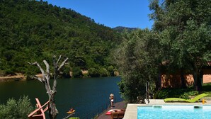 Zona de piscina con vistas a un lago y colinas boscosas.