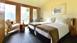 Un dormitorio con dos camas, una silla de madera, una mesita con una botella y vistas al exterior.