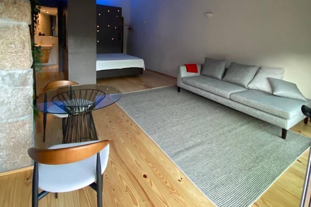 Una sala de estar moderna con un sofá, una mesa de comedor con sillas y una pequeña cocina visible a través de un vano abierto.