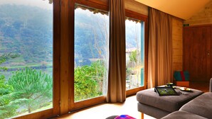Habitación con amplias ventanas que ofrecen vistas a un paisaje montañoso, un sofá y una tableta sobre una mesita.