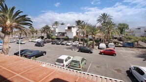 Un parking avec plusieurs voitures, des palmiers et des bâtiments en arrière-plan.