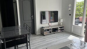 A modern living room with a dining table, chairs, a TV, and a sliding glass door leading to an outdoor area. - Petit Villa Climatise A Moriani Plage (San-Nicolao)