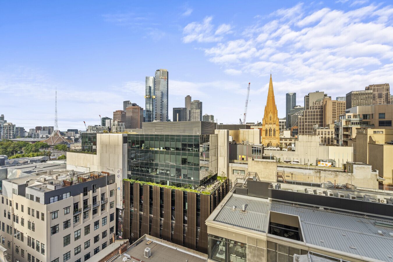 Une vue urbaine avec des bâtiments modernes, le clocher d’une église et une grue de chantier.