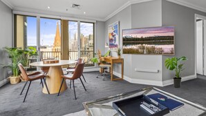 A modern hotel room with a large window, a dining area, a desk, and a mounted painting. - Bright, Luxury Penthouse with Amazing Views (Melbourne)