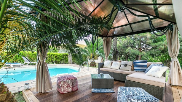 A covered outdoor seating area with a pool, wooden deck, and a sofa with patterned cushions. - Villa Euphoria Theologos Thassos (Θεολόγος)