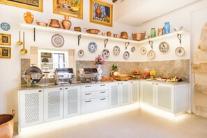 Een keuken met witte kastjes, een granieten aanrechtblad en diverse keukenapparaten. Er staan planken met koperen kookgerei en decoratieve borden.