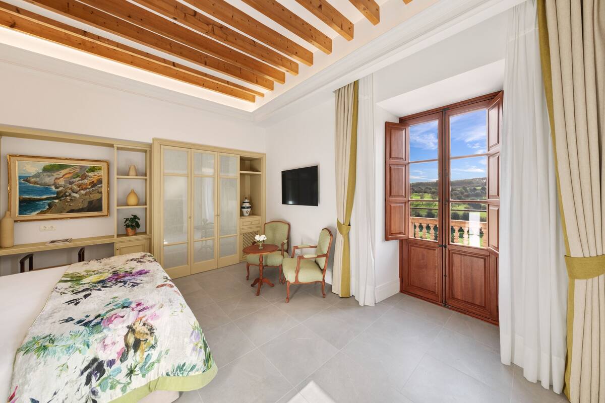 Une chambre à coucher avec un lit, un bureau, une chaise, un téléviseur et une fenêtre avec des rideaux.