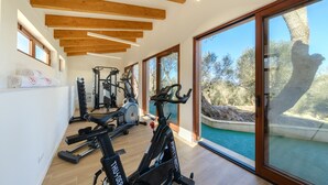 Une salle de sport moderne, équipée de machines de musculation, dotée de grandes fenêtres et offrant une vue sur une piscine.