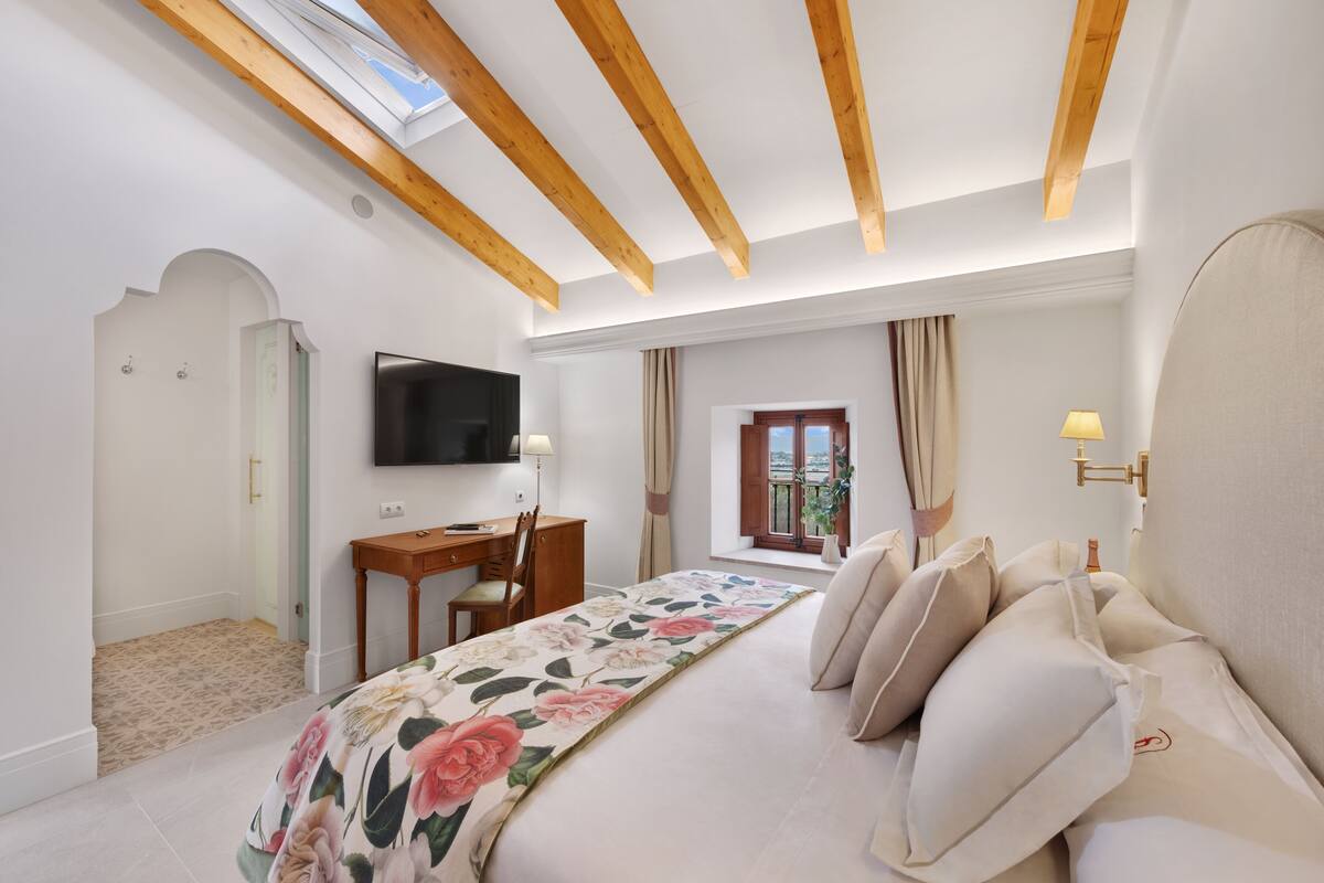 Une chambre à coucher avec un lit, un bureau, une chaise, un téléviseur et une fenêtre avec des rideaux.