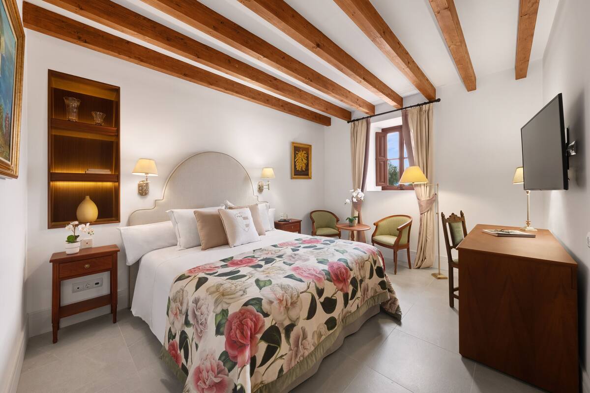 Une chambre à coucher comprenant un lit, des tables de chevet, un bureau, une chaise, un téléviseur et une fenêtre avec des rideaux.