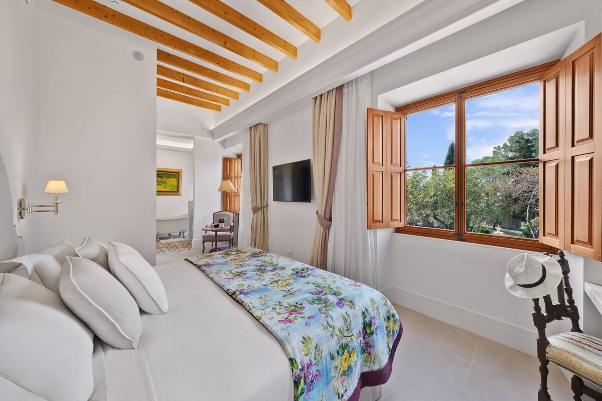 Une chambre à coucher avec un lit, une chaise, un téléviseur et une fenêtre avec des rideaux.