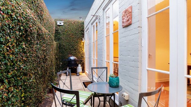 Eine Terrasse mit Tisch, Stühlen, einem Grill und einer Hecke.