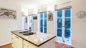 Eine moderne Küche mit Granit Arbeitsplatte, integriertem Geschirrspüler und Spüle. Große Fenster mit blaue Fensterläden, und eine Uhr an der Wand.