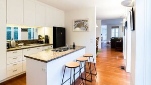 Eine moderne Küche mit weißen Schränken, Granit Arbeitsplatten, einem schwarzen Kühlschrank und einer kleinen Bar mit Hockern.