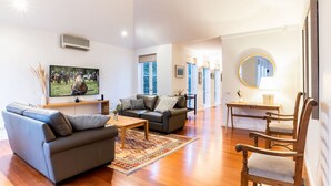 Ein geräumiges Wohnzimmer mit einem großen Flachbildfernseher, Ledersofas, einem Holztisch und einem Holzstuhl.
