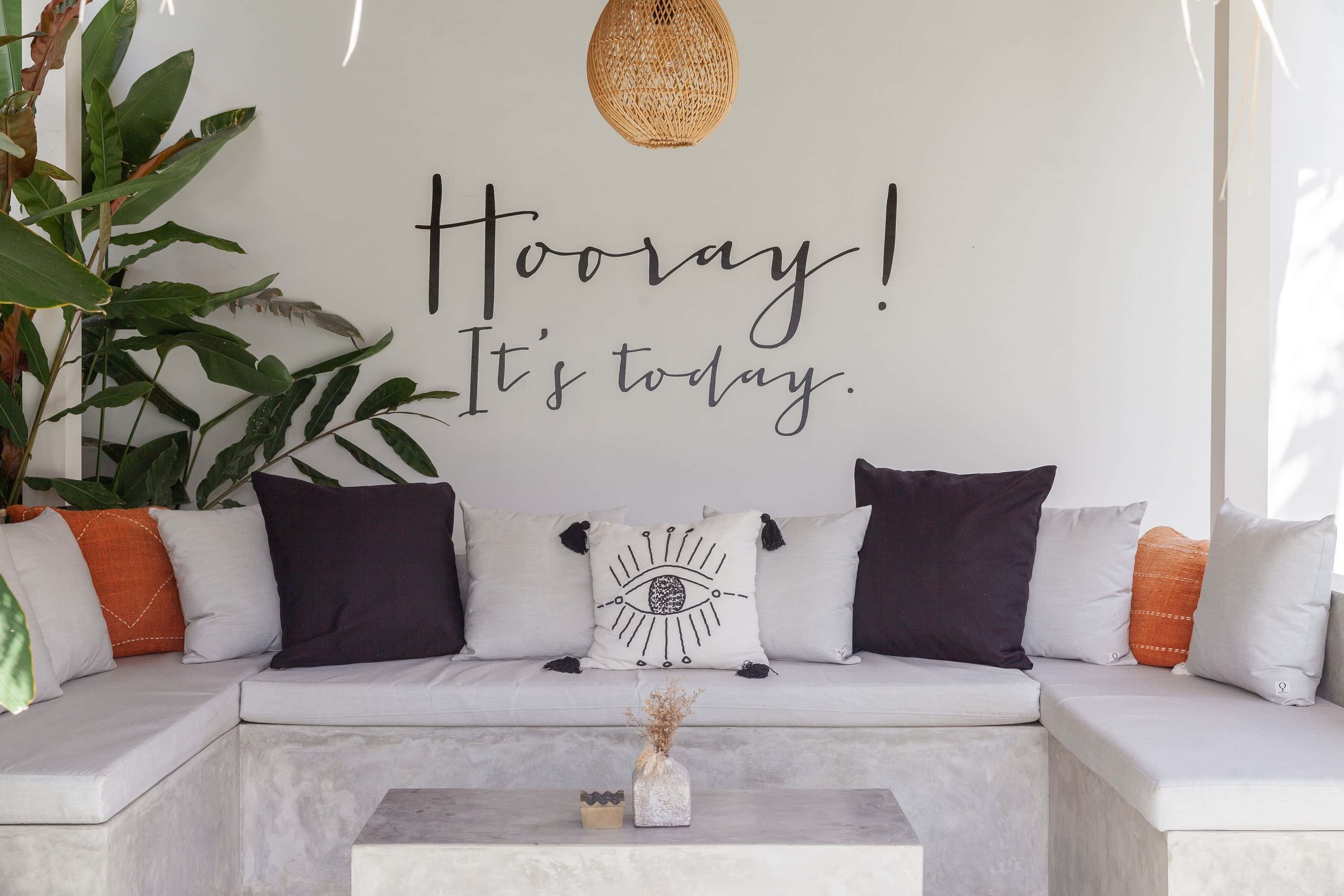 Un salon moderne avec un canapé blanc, des coussins décoratifs et un mur orné d’une citation inspirante.