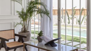 Ein Zimmer mit großem Fenster, Topfpflanze, Leseständer und Blick auf Pool und Außenbereich.