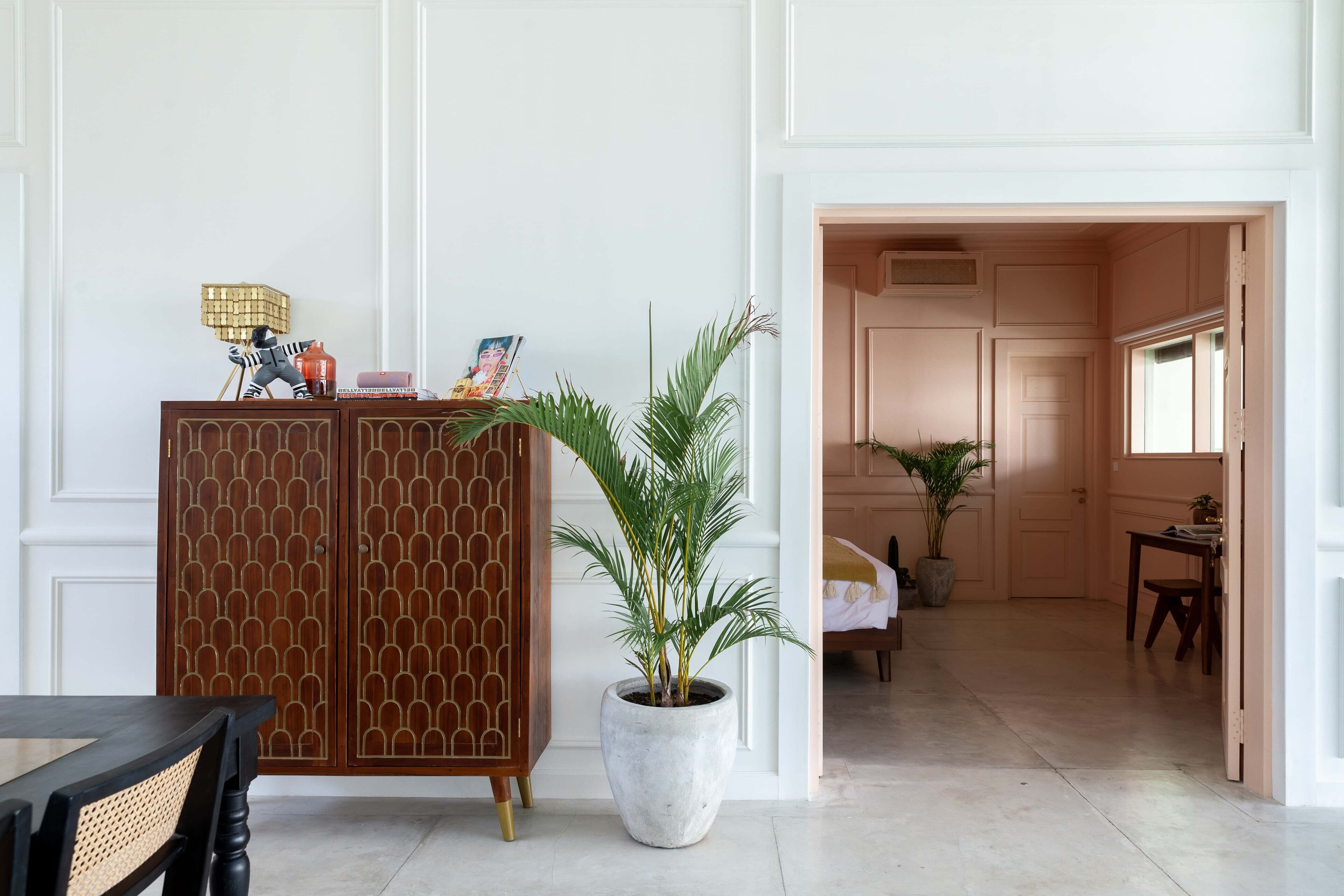 Une pièce comprenant un meuble en bois, une grande plante en pot, une table à manger et une porte donnant sur une autre pièce.